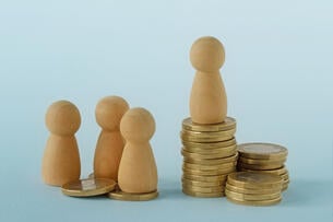 A photo of chess pawn–like figures on stacks of coins of varying heights, suggesting income inequality.