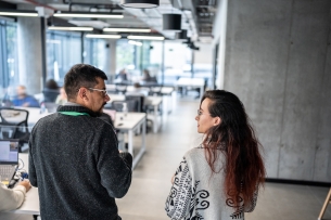 An older professional walks alongside a younger intern through an office
