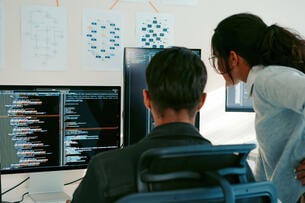 Two adults work on a computer looking at web code