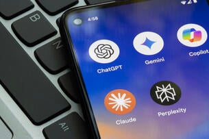 A close-up of a smartphone, lying atop a computer keyboard, with icons for generative AI apps ChatGPT, Gemini, Copilot, Claude and Perplexity visible on the screen.