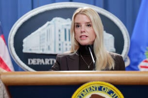 U.S. Attorney General Pam Bondi, a white woman with blond hair wearing a black turtleneck, speaks at a podium.
