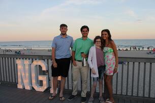 Four young people stand on a patio in front of a beach sunset